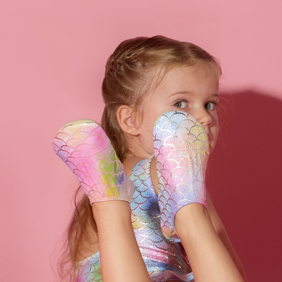 Child wearing colorful Finny Shoes mermaid scale-themed shoes against a pink background